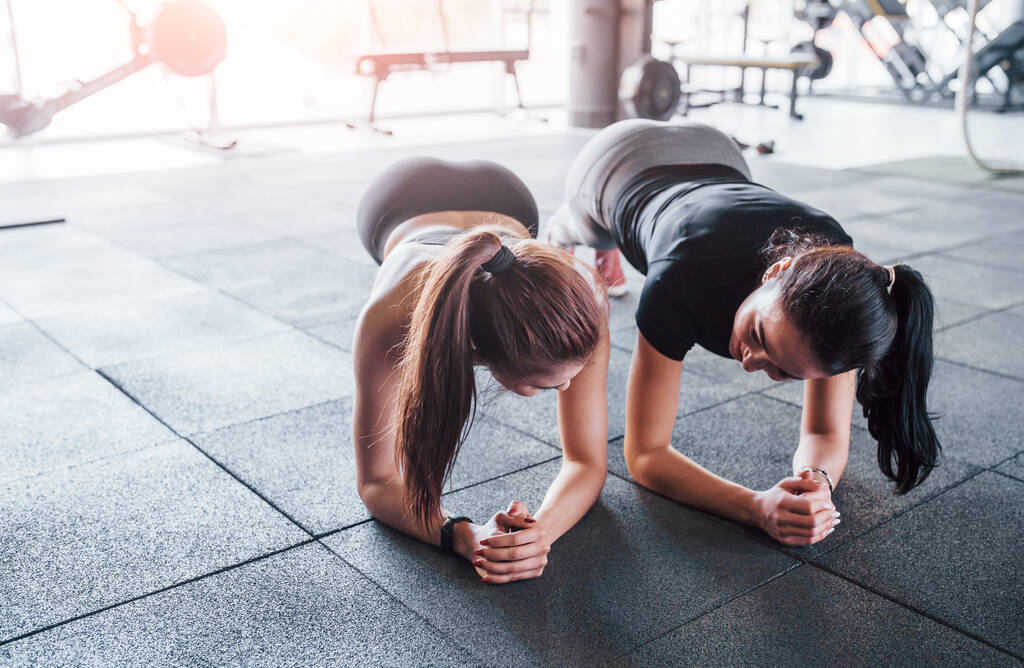Dvě mladé dívky ve sportovním oblečení je v tělocvičně dělat cvičení společně. - Fotografie, Obrázek