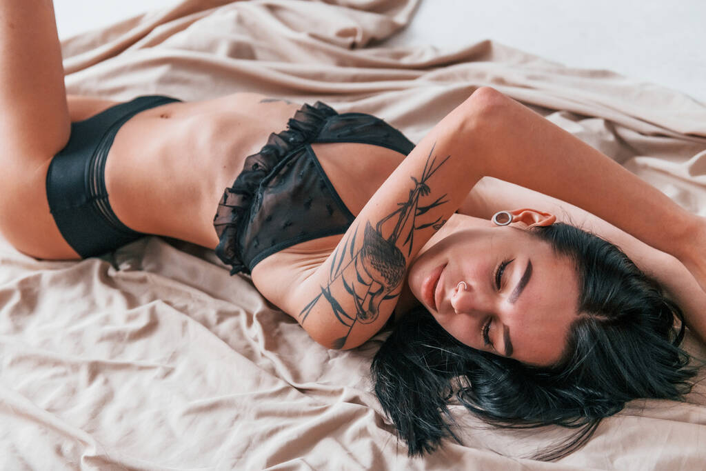Sexy bruna attraente in biancheria intima nera e con tatuaggi sul corpo è sdraiato sul pavimento. - Foto, immagini