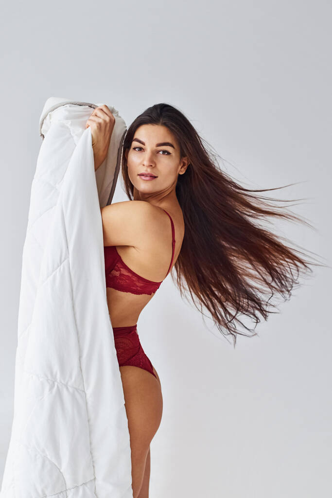 Женщина в красном нижнем белье покрывает свое тело полотенцем в студии на белом фоне. - Фото, изображение