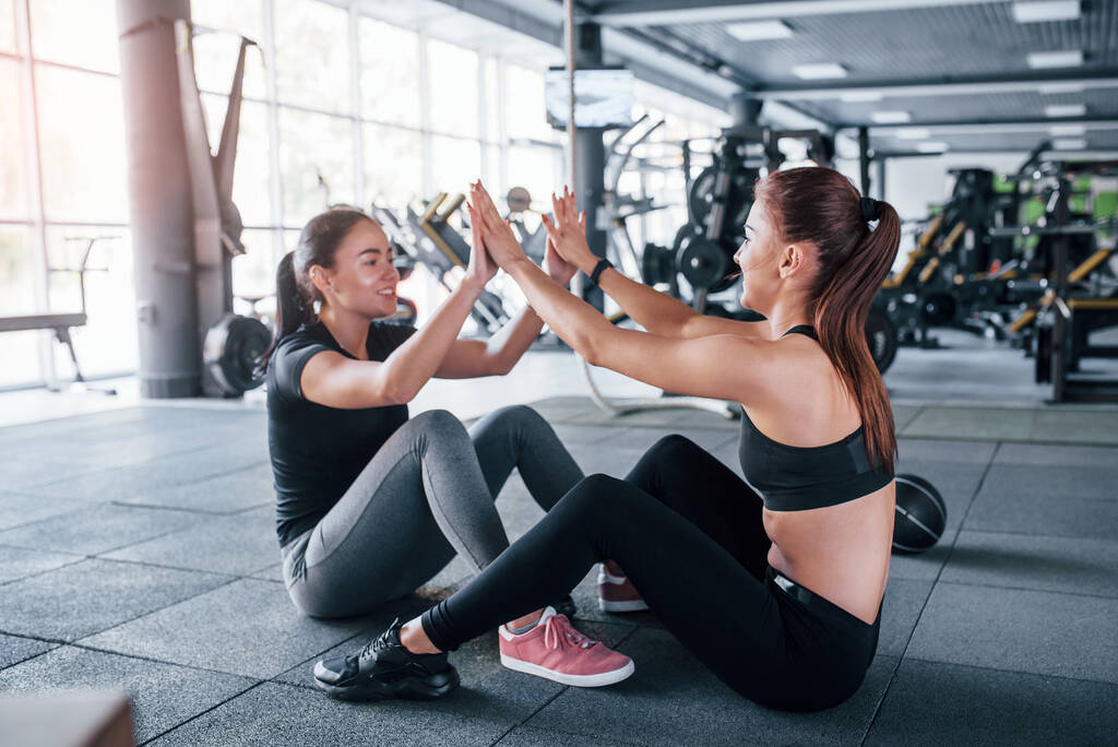 Two young girls in sportive clothes is in the gym doung workout together. - Photo, Image