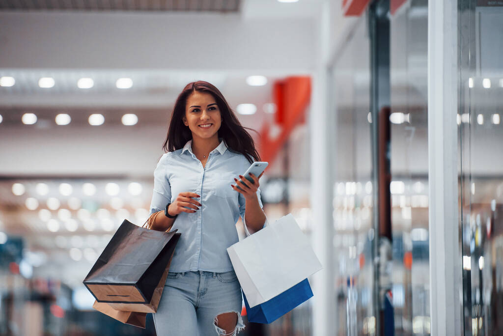Bruna donna al supermercato con molti pacchetti e telefono in mano hanno giornata di shopping. - Foto, immagini