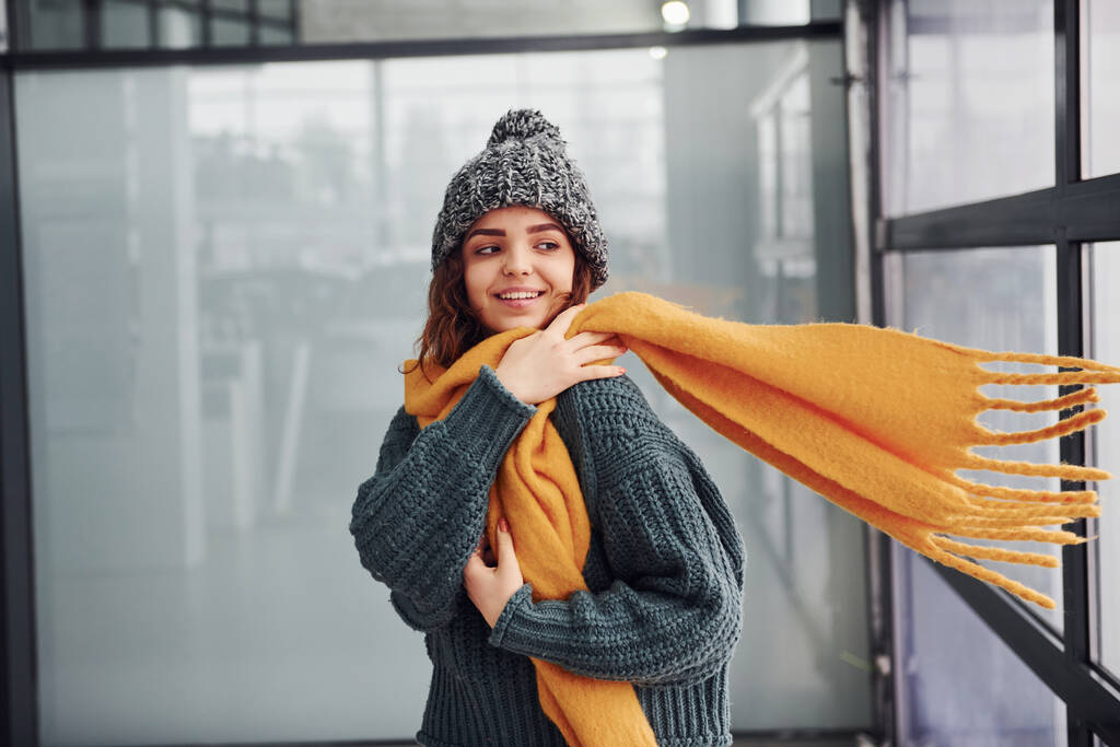 Beautiful cheerful girl in yellow scarf and in warm clothes standing indoors. - Photo, Image