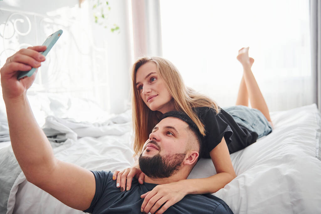 Giovane coppia sposata fare un selfie utilizzando il telefono in camera da letto durante il giorno. - Foto, immagini