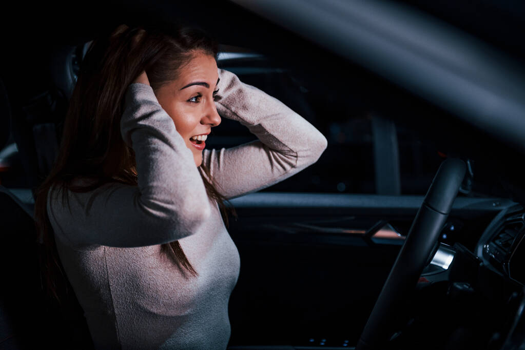 Vista lateral de la mujer joven que gestos dentro de un automóvil moderno a estrenar. - Foto, imagen