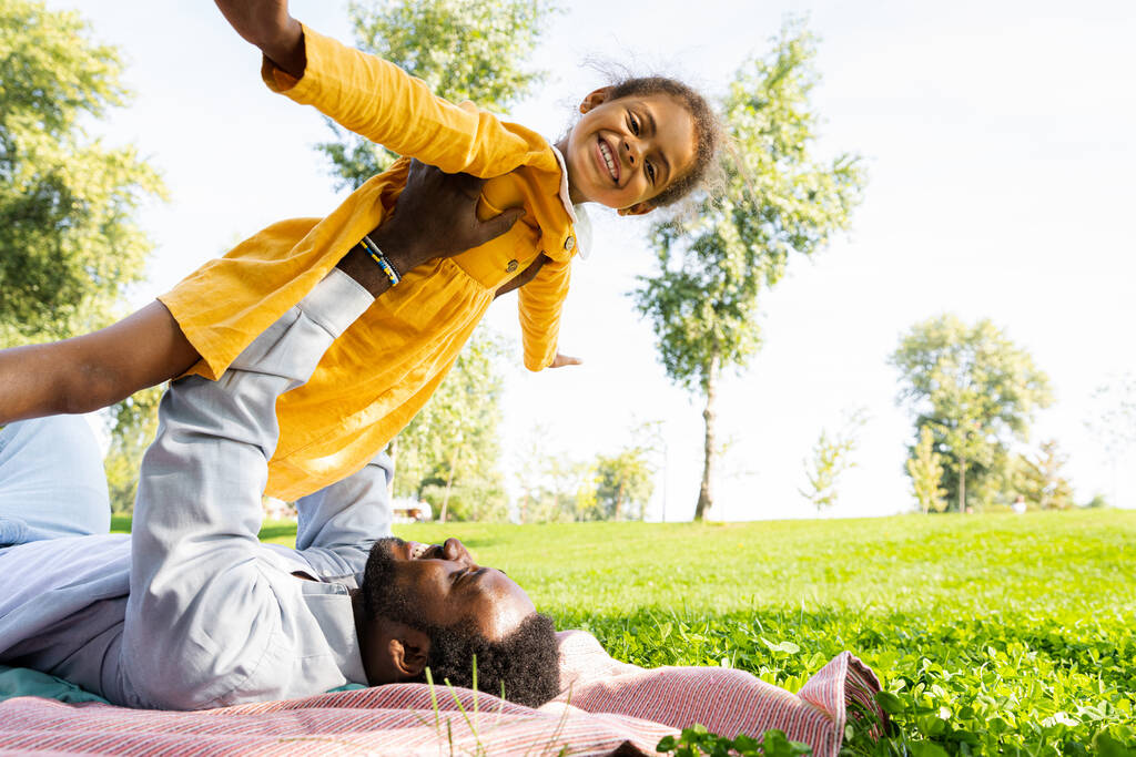 公園で美しい幸せなアフリカ系アメリカ人の家族の絆-屋外で楽しい時間を過ごしている黒人家族、かわいい娘と遊ぶお父さん - 写真・画像