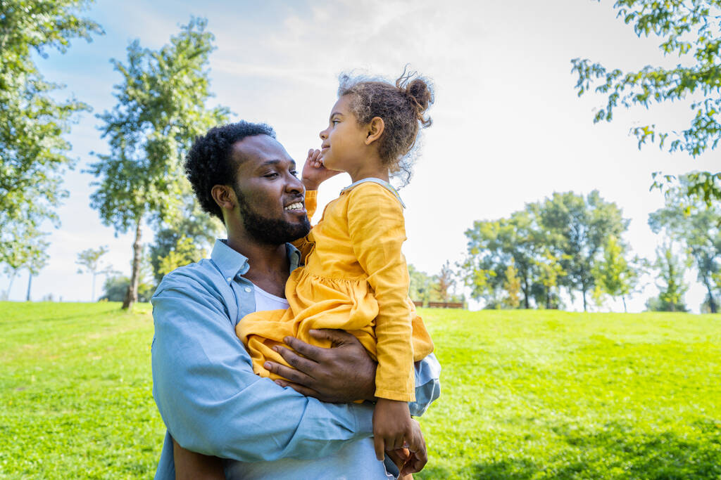 Mooi gelukkig Afrikaans amerikaans familie binding in het park - zwart familie plezier hebben buiten, papa spelen met zijn schattige dochter - Foto, afbeelding