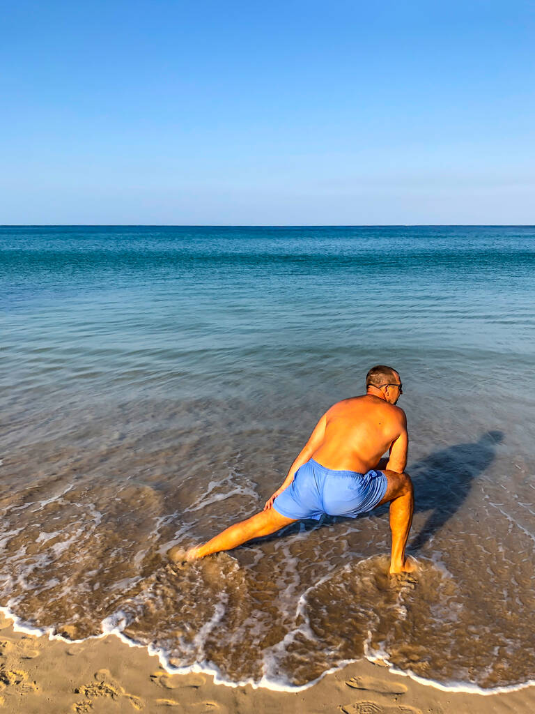 Ένας άντρας πηγαίνει για σπορ, κάνει ασκήσεις στην παραλία. - Φωτογραφία, εικόνα