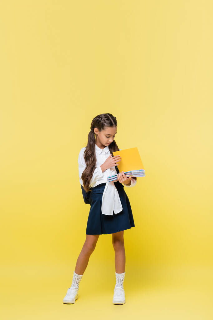 Studentessa holding notebook mentre in piedi su sfondo giallo  - Foto, immagini