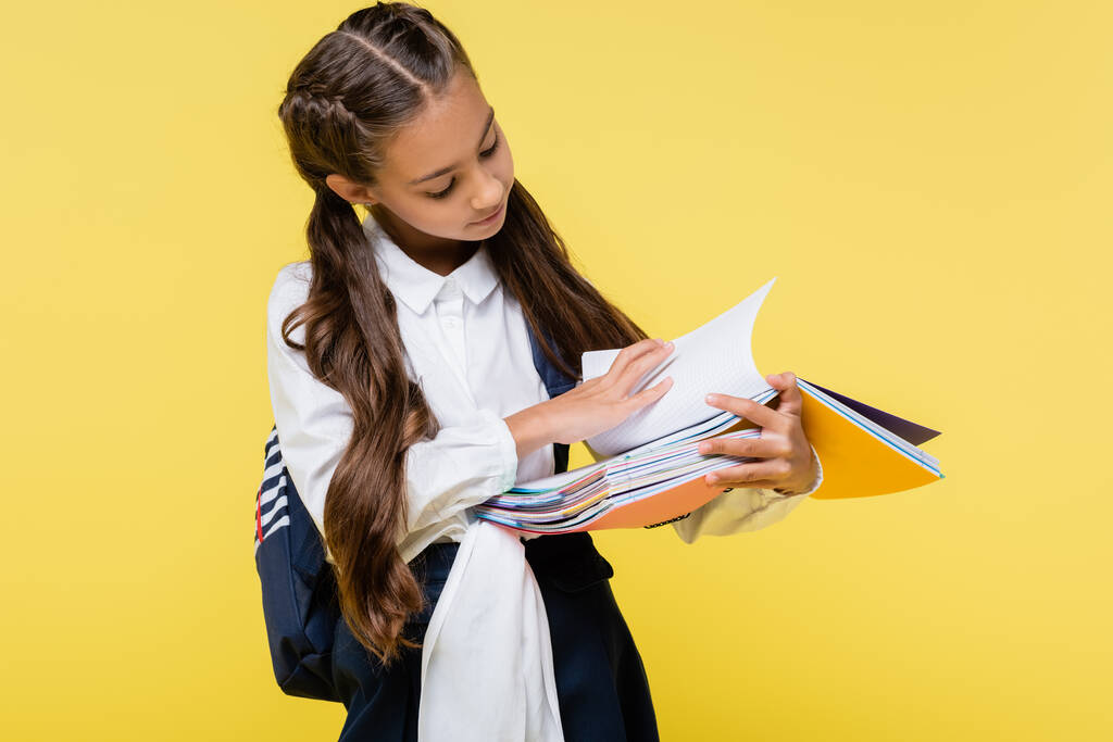 Schoolkind met rugzak op zoek naar notebooks geïsoleerd op geel - Foto, afbeelding