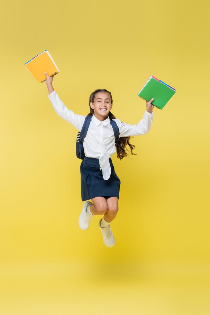 Feliz colegial con mochila y cuadernos saltando en amarillo - Foto, imagen