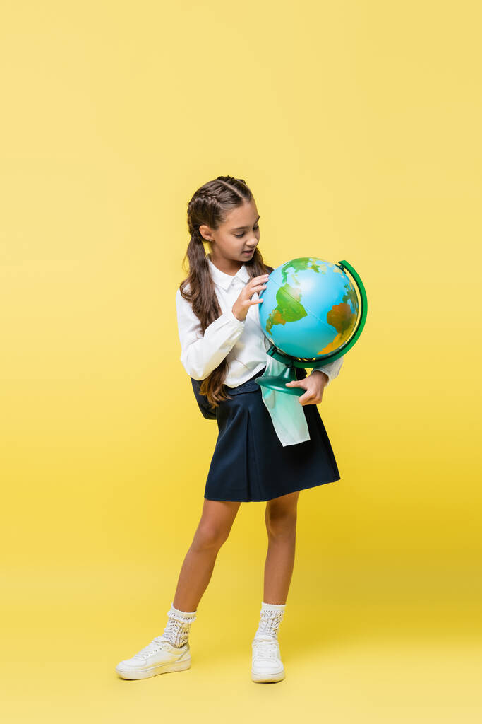 Schoolkind met rugzak holding globe op gele achtergrond  - Foto, afbeelding