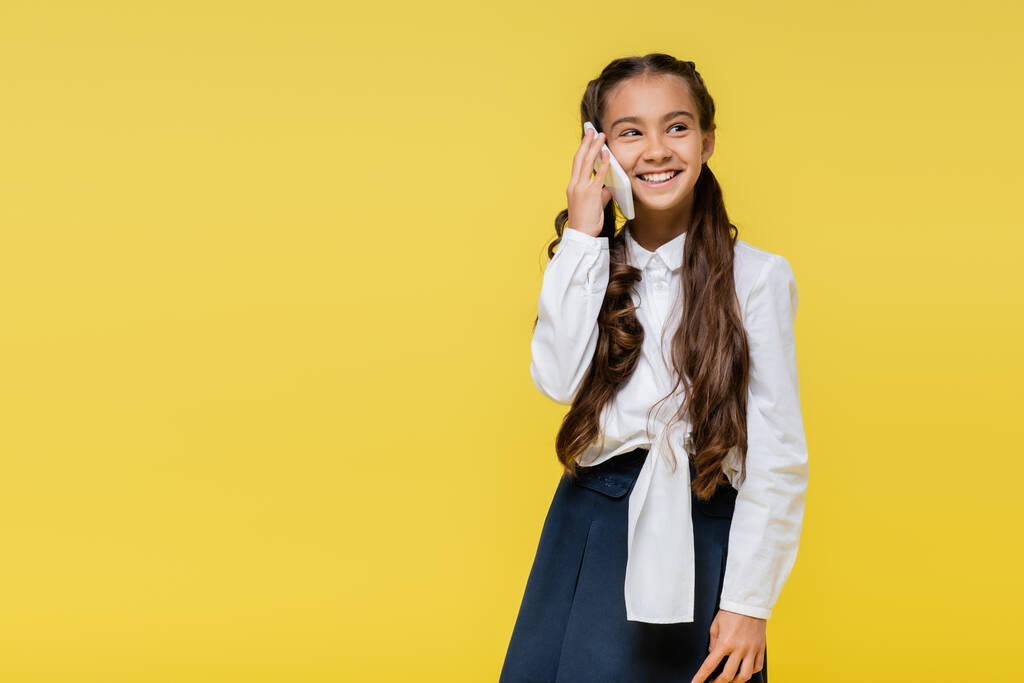 Hymyilevä koululainen puhuu matkapuhelimella keltaisella taustalla kopiotilaa - Valokuva, kuva