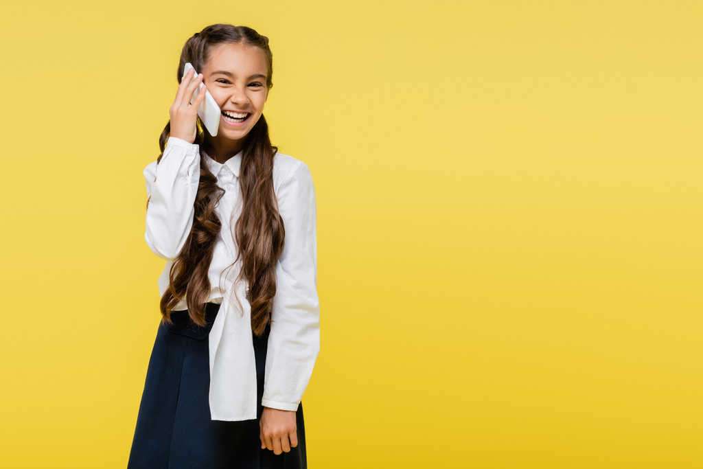 Весела школярка розмовляє на мобільному телефоні ізольовано на жовтому
  - Фото, зображення
