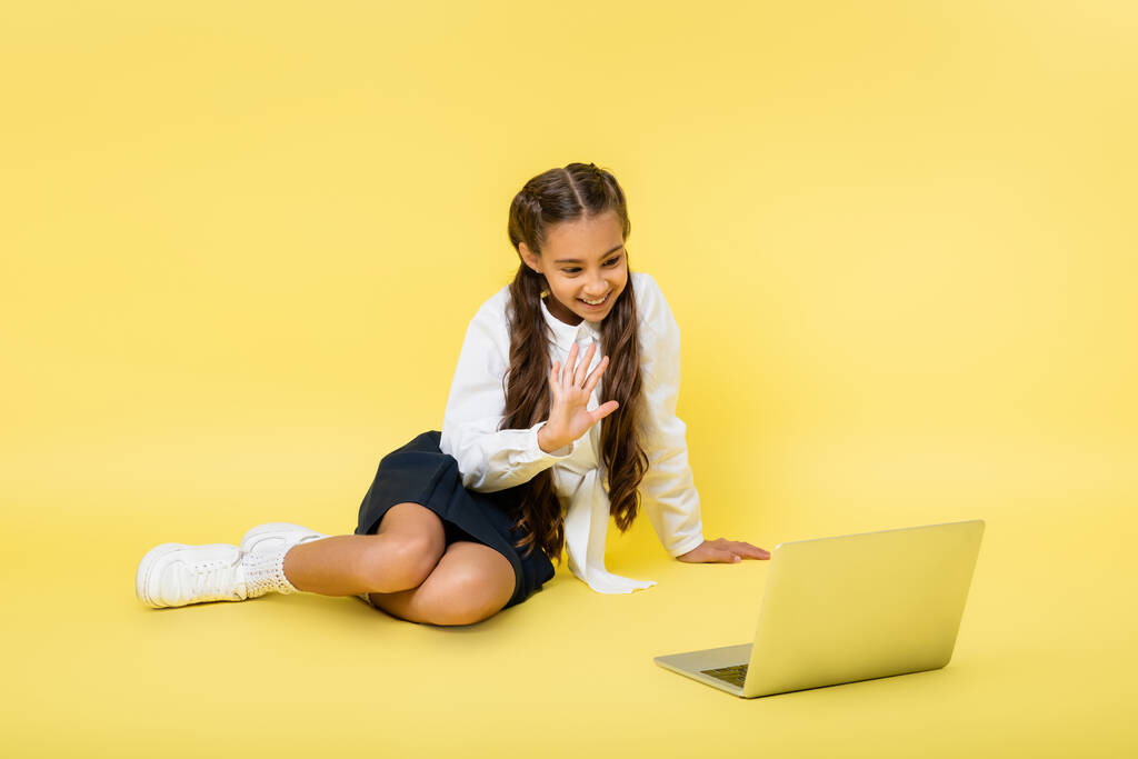 Écolière souriante ayant appel vidéo sur ordinateur portable sur fond jaune - Photo, image