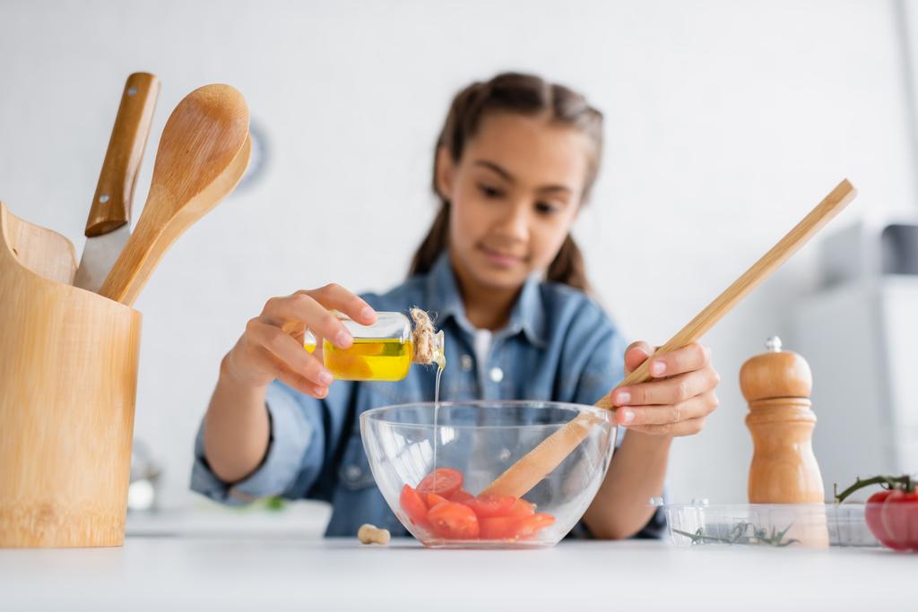Размытая девушка наливает оливковое масло в миску с помидорами черри на кухне  - Фото, изображение