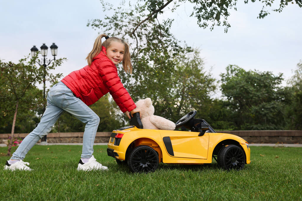Cute little girl playing with toy bear and children's car in park - Photo, Image
