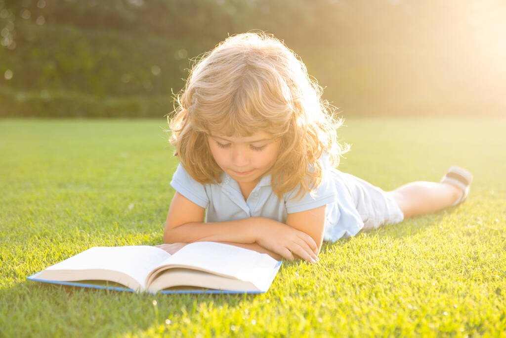 Mądre dzieciaki. Mały chłopiec czyta książkę w letnim świetle zachodu słońca. Letnia edukacja dzieci na świeżym powietrzu. - Zdjęcie, obraz