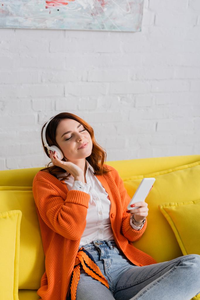 mosolygós nő fülhallgató gazdaság smartphone miközben zenét hallgat csukott szemmel - Fotó, kép