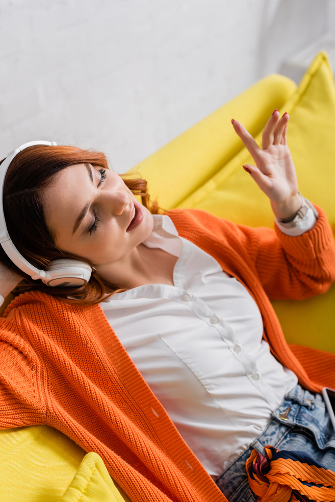 freudige Frau mit geschlossenen Augen gestikuliert beim Musikhören über Kopfhörer - Foto, Bild