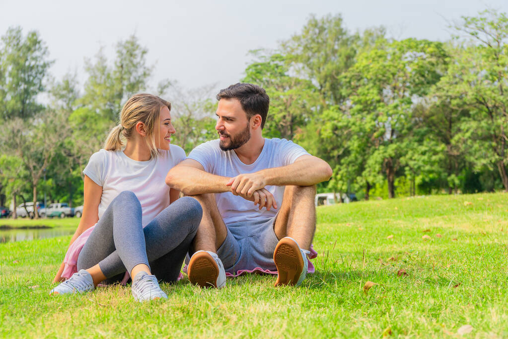 caucasian athletic couple in sportswear sitting for relax together after work out outdoors in park in summer. - Photo, Image