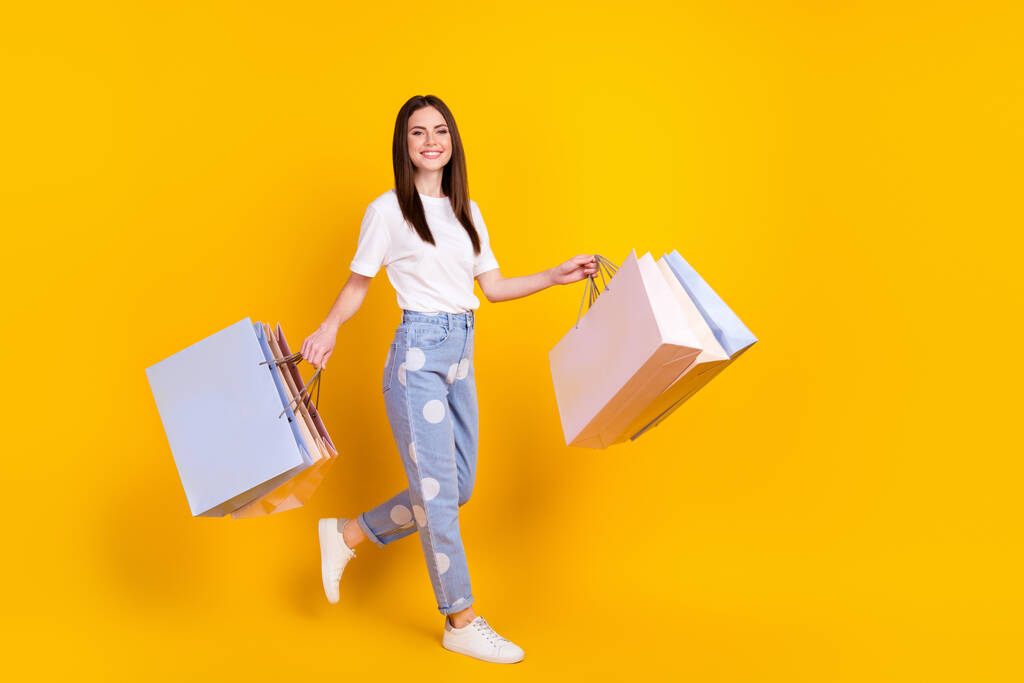 Teljes méretű profil oldalán fotó boldog pozitív lány shopaholic hold bevásárló táskák elszigetelt sárga színű háttér - Fotó, kép