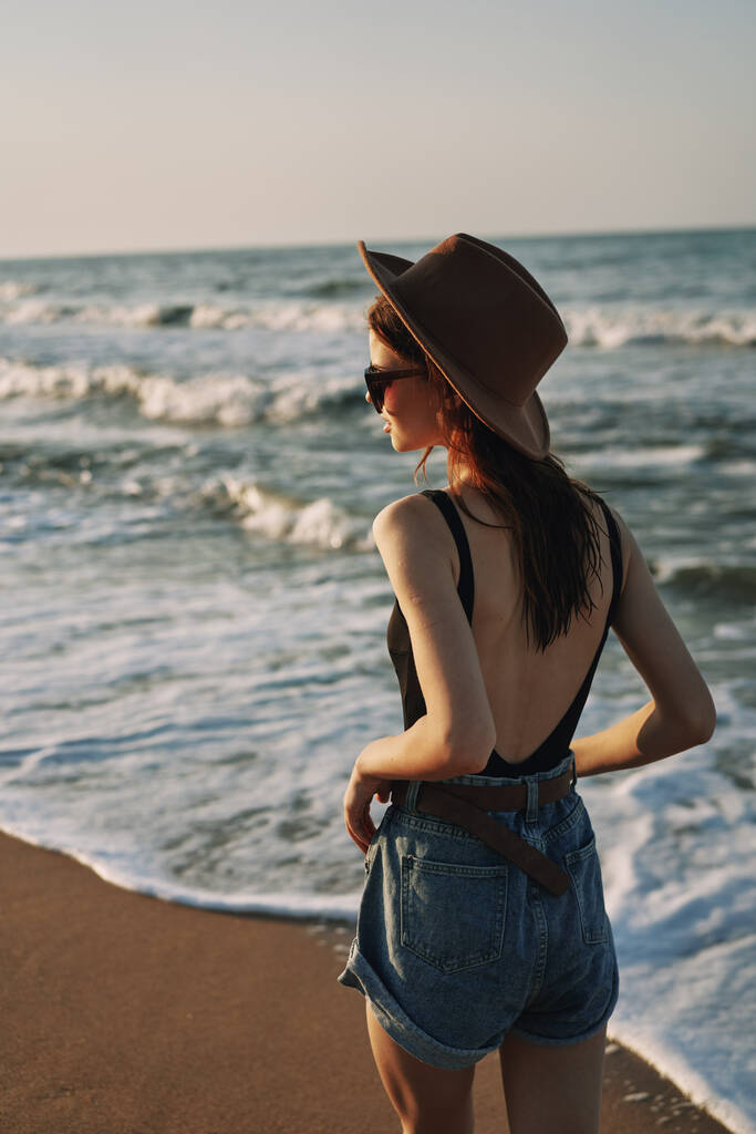 Fröhliche Frau mit Sonnenbrille und Hut geht am Meer entlang - Foto, Bild