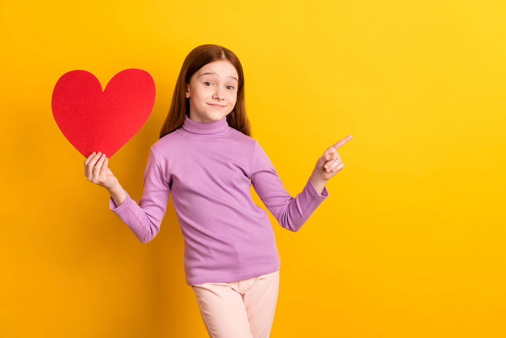Portret van mooi trendy vrolijk meisje in handen grote hartkaart tonen kopieerruimte geïsoleerd over helder gele kleur achtergrond - Foto, afbeelding