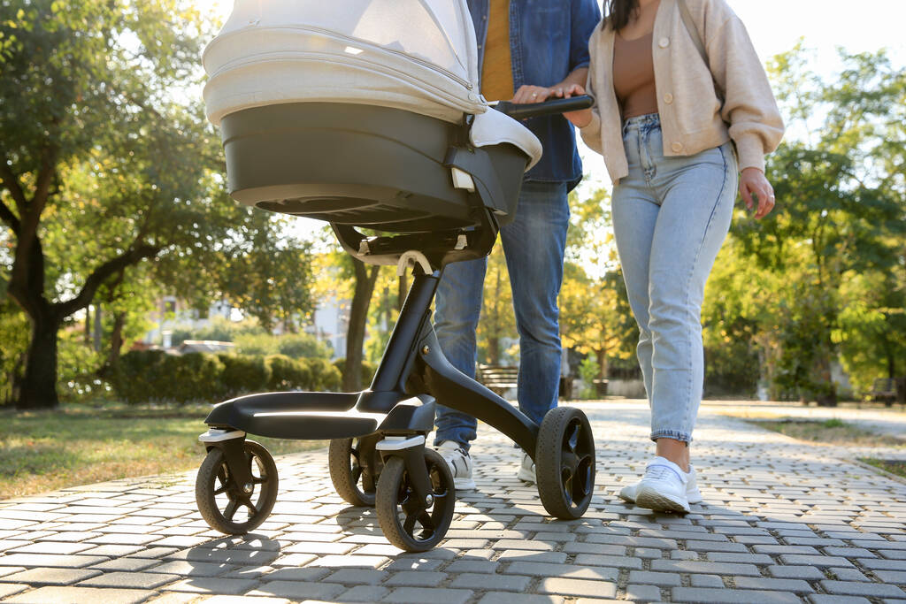Родители, гуляющие со своим ребенком в коляске в парке в солнечный день, крупный план - Фото, изображение