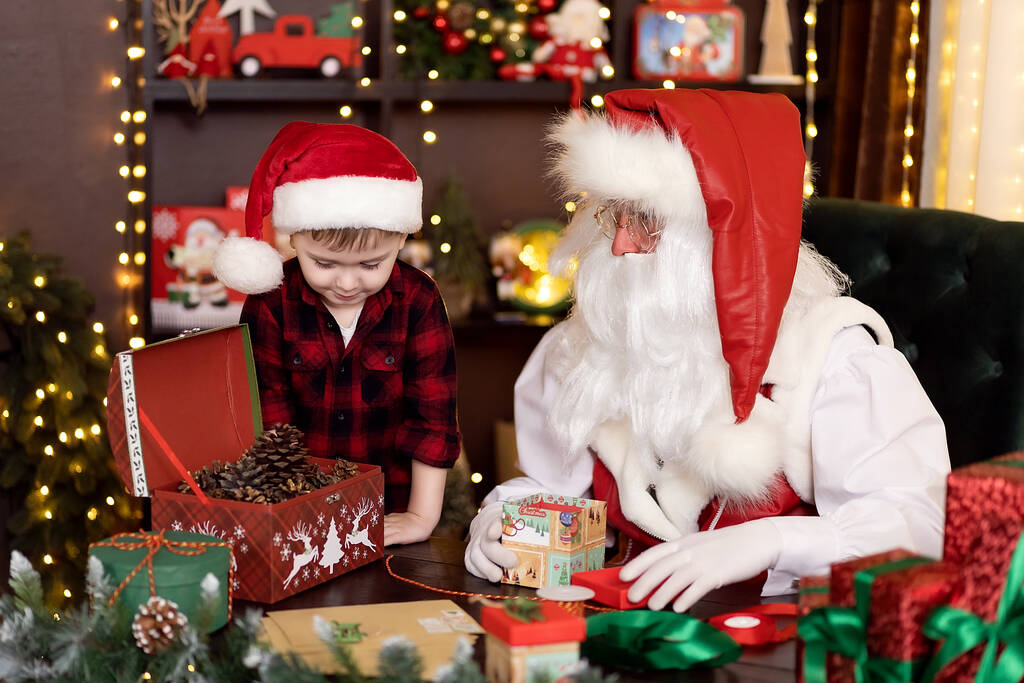 Санта-Клаус с маленьким помощником мальчика упаковки рождественские подарки для детей. НОВОГОДОВОЙ КОНЦЕПТ - Фото, изображение
