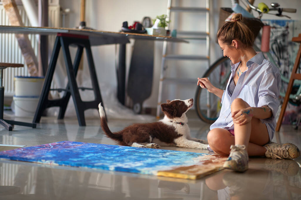 Junge verführerische Künstlerin spielt mit ihrem Hund im Atelier - Foto, Bild