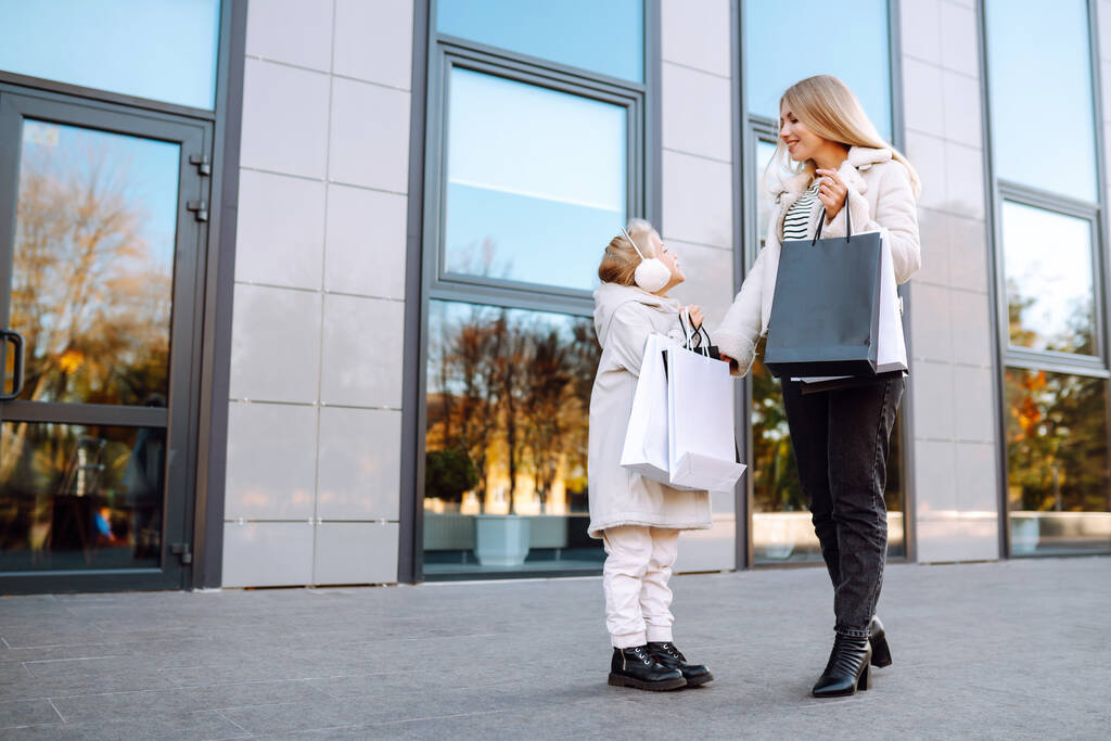 Mladá matka a roztomilé dítě s nákupními taškami po nakupování. Černý pátek. Spotřebitelství, nákupy, prodej, životní styl, cestovní ruch. - Fotografie, Obrázek