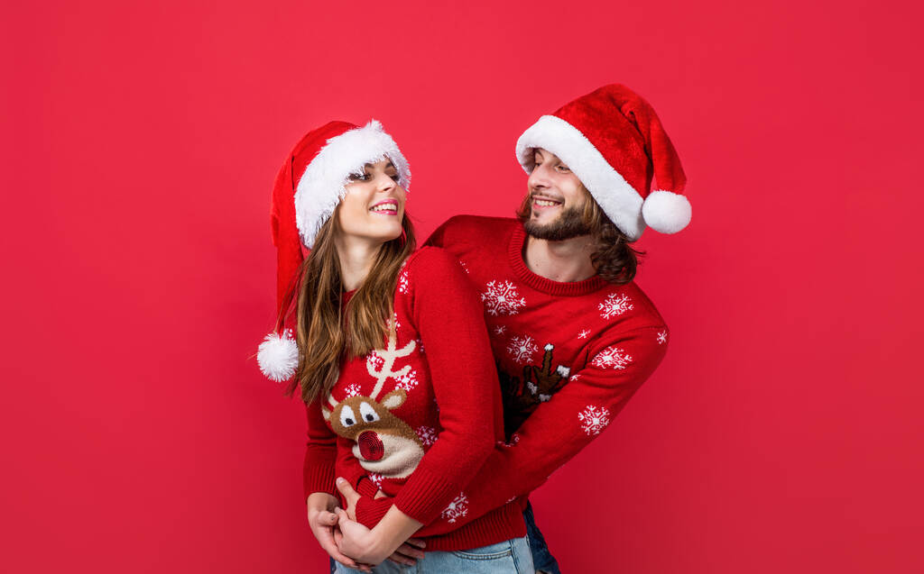 C'est Noël. heureux nouveau couple de l'année en pull tricoté et santa claus chapeau. Préparez-vous pour la fête de Noël amusant. Joyeuses vacances pour les jeunes familles. homme et femme sur fond rouge. amour - Photo, image