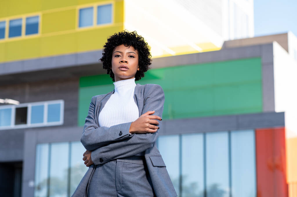 Una joven dama afroamericana cool con el pelo rizado vestido profesionalmente posando cerca de edificios - Foto, Imagen