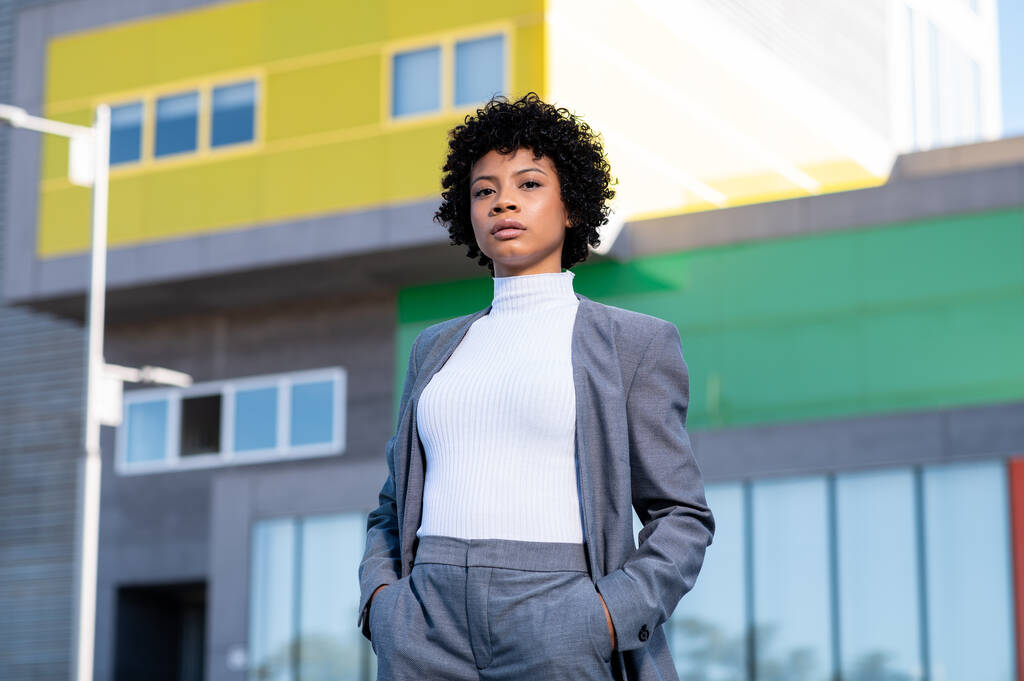 Une jeune afro-américaine fraîche aux cheveux bouclés habillée professionnellement posant près des bâtiments - Photo, image