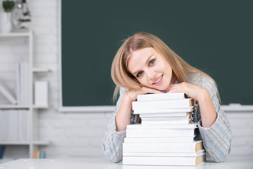 Κοντινό πλάνο πορτρέτο της ευτυχούς ελκυστική νεαρή μαθήτρια με τα βιβλία στον πίνακα στην τάξη. - Φωτογραφία, εικόνα