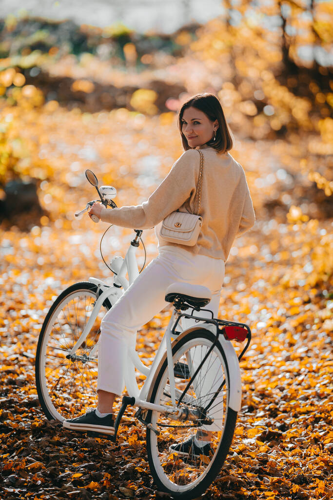 Kaunis muotokuva nainen pyöräily yksin syksyllä puistossa. Aurinkoinen päivä, kultaisia lehtiä metsässä. Trendikäs nainen vintage valkoinen polkupyörä, terveellinen elämäntapa, esteettinen kohtaus - Valokuva, kuva