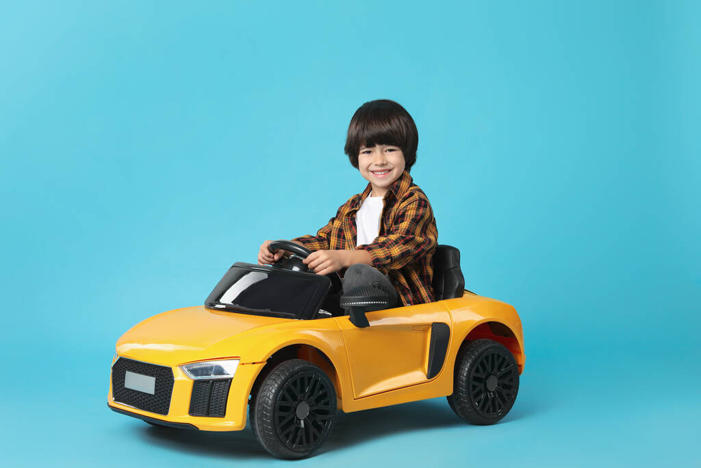 Açık mavi arka planda sarı oyuncak araba kullanan küçük çocuk. - Fotoğraf, Görsel