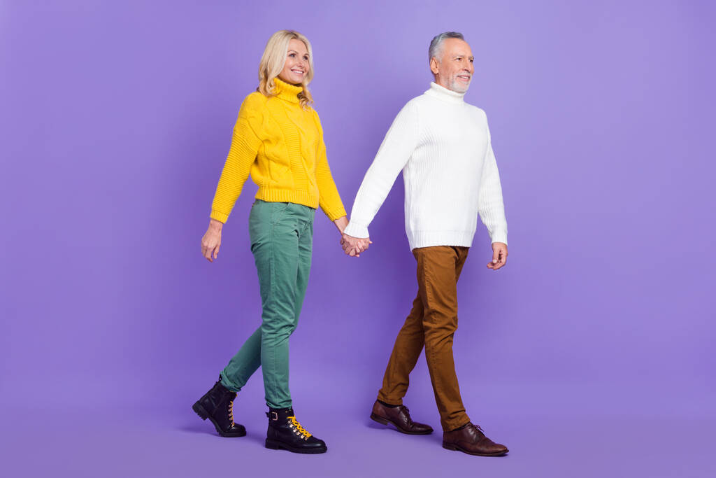 Φωτογραφία από αστείο χαριτωμένο ηλικιωμένος σύζυγος σύζυγος ντυμένη πλεκτά πουλόβερ περπάτημα κρατώντας τα χέρια αναζητούν κενό χώρο απομονωμένο βιολετί χρώμα φόντο - Φωτογραφία, εικόνα