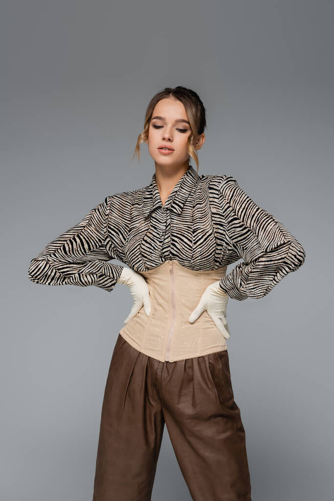 стильная женщина в блузке с отпечатком зебры, позирующая руками на бедрах, изолированных на сером - Фото, изображение