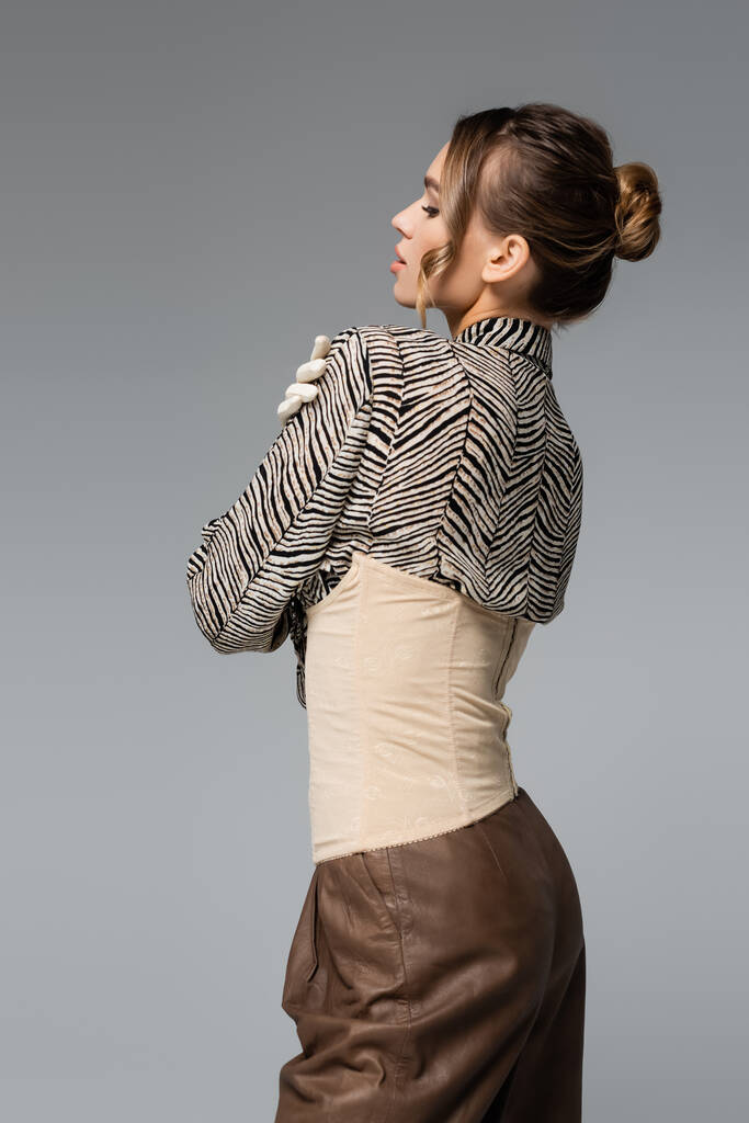 молода жінка в блузці з тваринним принтом і бежевим корсетом позує ізольовано на сірому
 - Фото, зображення