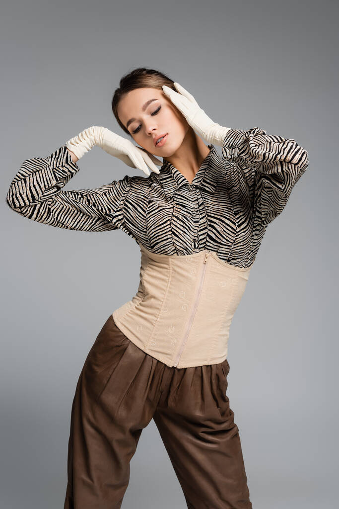 Trendfrau in Bluse mit Animal Print, Handschuhen und Korsett posiert isoliert auf grau - Foto, Bild