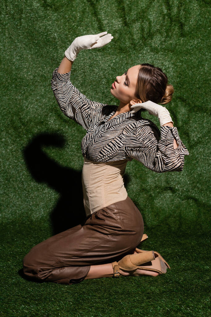 полная длина стильная женщина в блузке с зеброй печати жесты, сидя рядом травяной фон  - Фото, изображение
