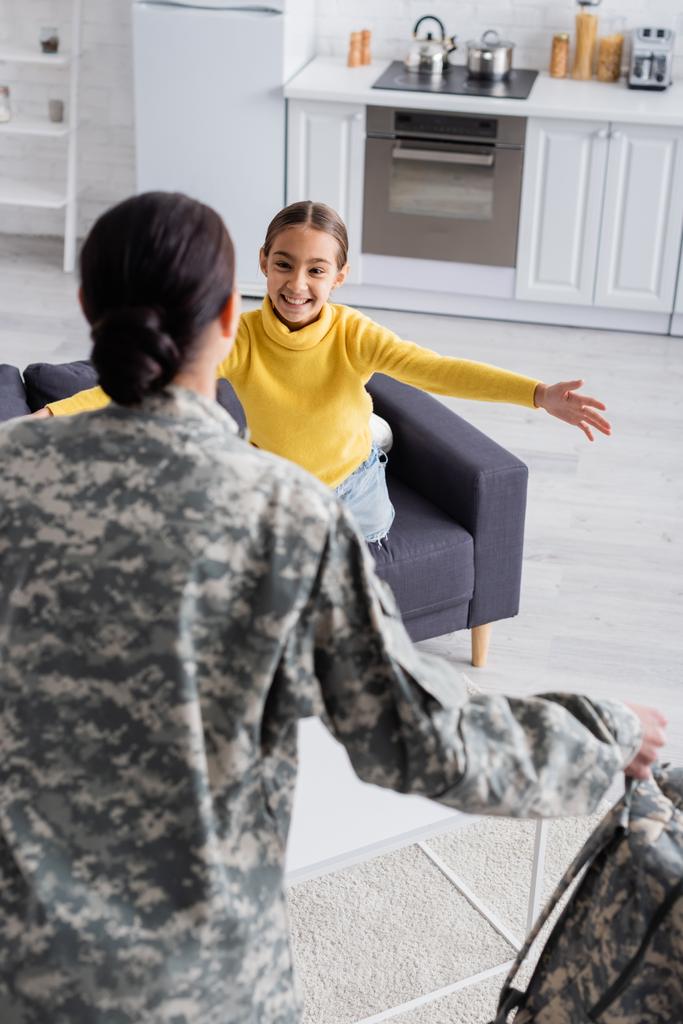Ragazzo preadolescente sorridente a mamma offuscata in uniforme militare a casa  - Foto, immagini