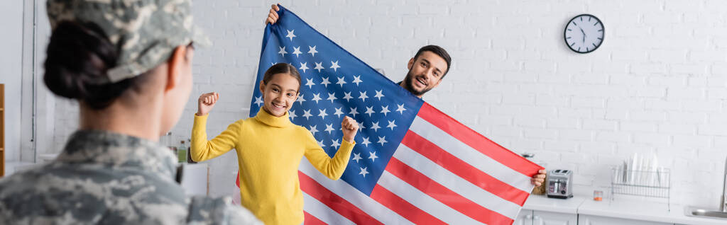 Onnellinen perhe, jossa Amerikan lippu katselee naista armeijan univormussa kotona, banneri  - Valokuva, kuva