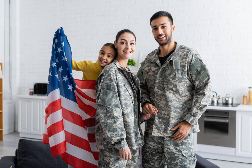 Parents in military uniform holding hands near preteen kid with american flag at home  - Photo, Image