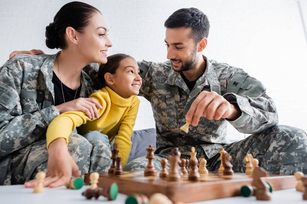 Glücklicher Mann in Militäruniform hält Schachfigur neben Tochter und Frau zu Hause  - Foto, Bild