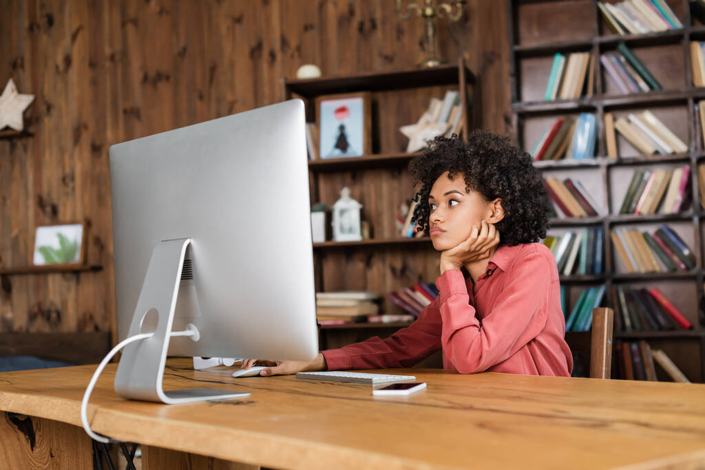 fiatal afro-amerikai nő számítógép egérrel, miközben nézi monitor otthon - Fotó, kép