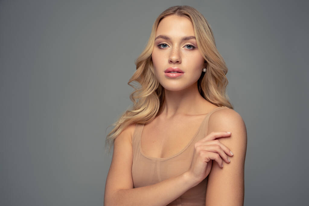 Portrait of a beautiful blonde with curly  long hair and in a beige top - Photo, Image