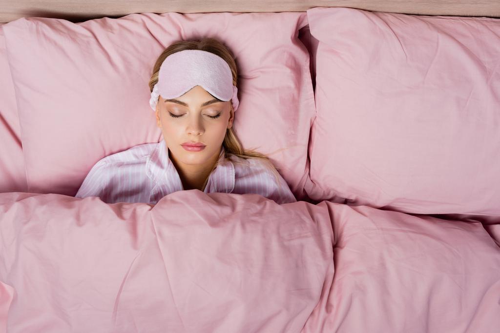 Widok z góry kobiety z maską śpiącej na różowej pościeli w domu - Zdjęcie, obraz