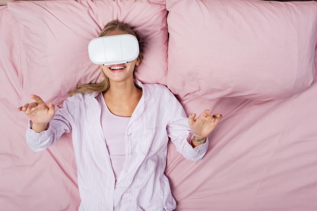 Top view of smiling woman using vr headset on bed at home  - Photo, Image